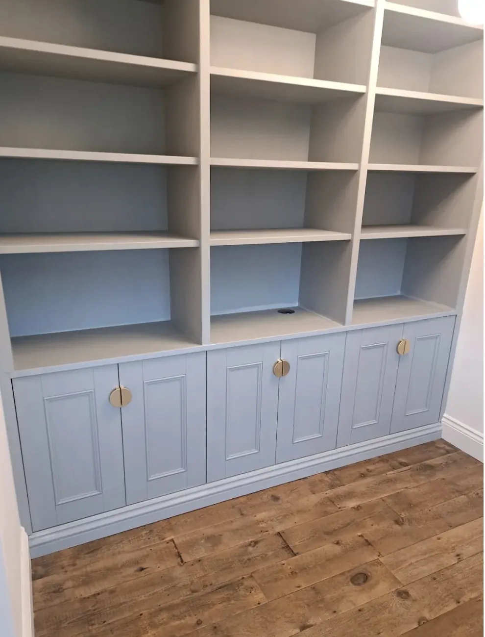 Fitted bookcase with open shelving above pale blue panelled cupboards