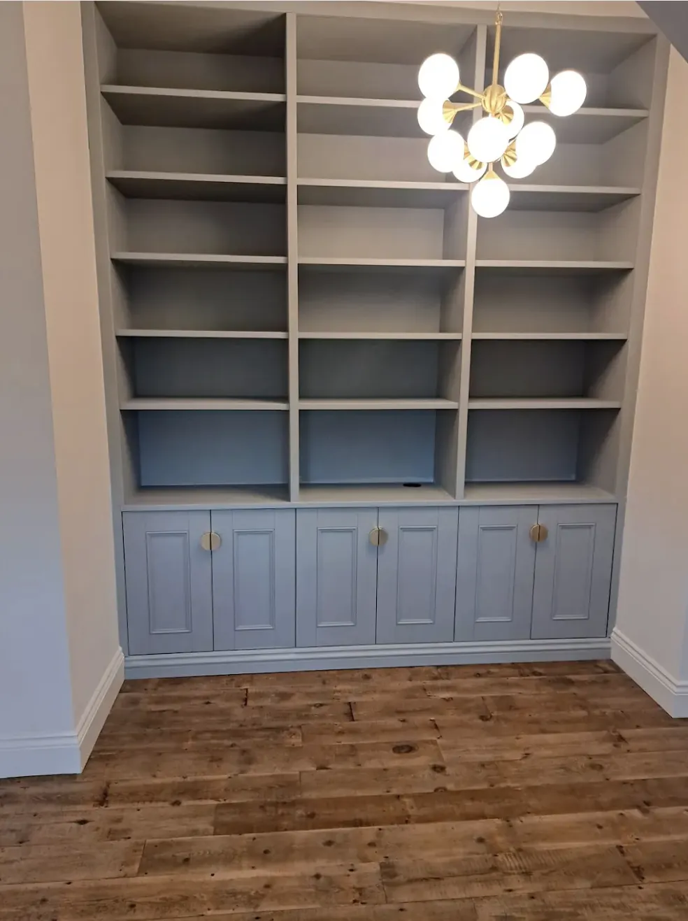 Full-height fitted alcove bookcase in pale blue with panelled cupboard doors below