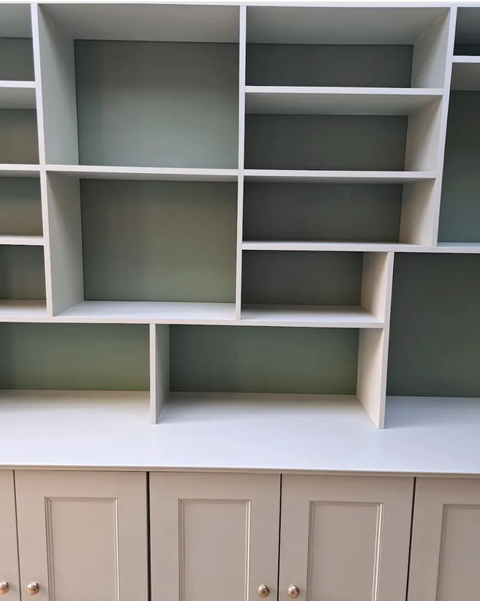 Close view of the asymmetric shelving grid, each bay a different width, in sage green and stone