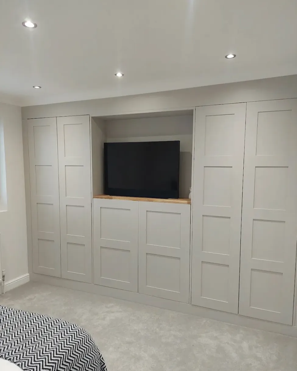 Wall of fitted shaker wardrobes with a central television recess and oak shelf